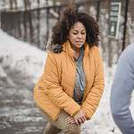 Serious black woman warming up with anonymous trainer in snowy park
