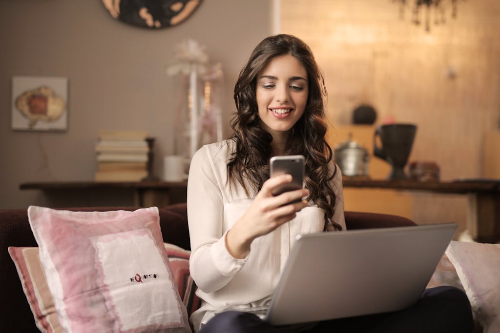 A woman using her smartphone and laptop in a cozy living room. The trap of comfort in a disconnected world