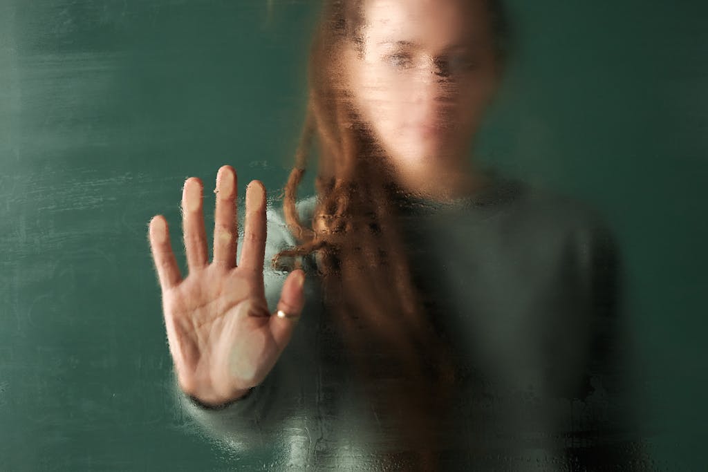 Blurred image of a woman with her hand pressed against a glass, trapped in the comfort and detachment from real life.